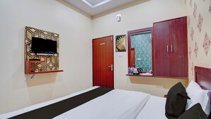 Habitación de hotel con cama, televisor montado en la pared, armario y una mesita con hervidor y botellas.