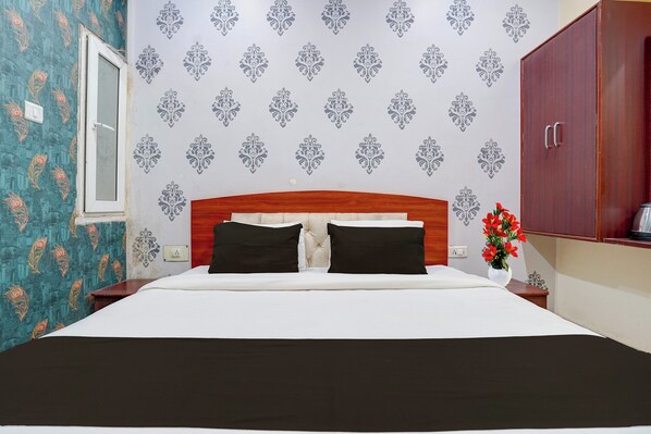 A hotel room with a bed, a wooden headboard, a nightstand, a vase with flowers, and a wardrobe. - Super Collection O Chet Singh Ghat (Varanasi)