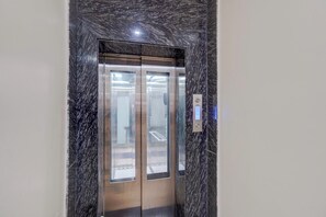 Un ascensor con detalles metálicos y una pared de aspecto marmolizado a su alrededor.