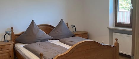 A bedroom with a wooden bed, two nightstands, a lamp, a window with blinds, and a ceiling light fixture.