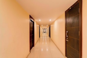A long, narrow hotel corridor with doors on both sides, a tiled floor, and recessed lighting.