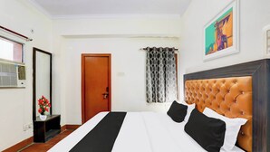 Quarto de hotel com uma cama, uma porta, uma janela com ar condicionado, um quadro na parede e uma cortina.