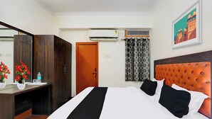 Quarto de hotel com cama, escrivaninha, guarda-roupa, ar condicionado e um quadro na parede.