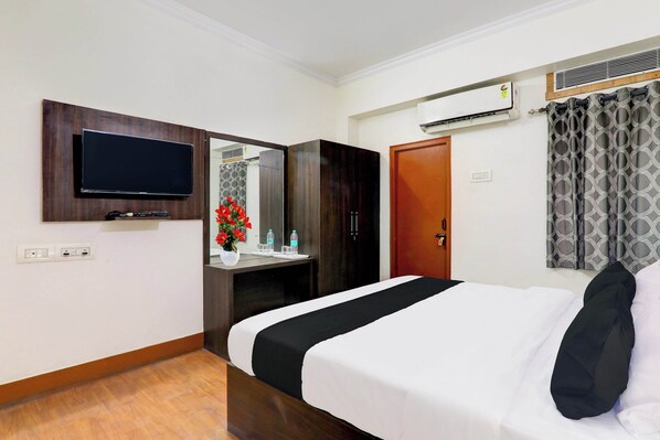 A hotel room with a bed, a television, a mirror, a wardrobe, and an air conditioning unit.