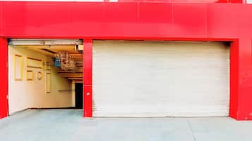 Un bâtiment rouge avec une porte de garage fermée et une porte ouverte donnant sur une pièce ornée d’un lustre.
