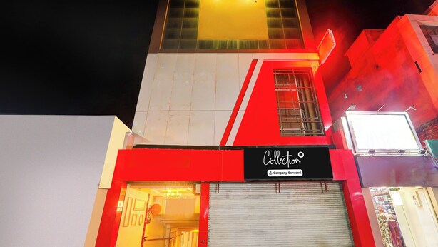 Um edifício com fachada marcante em vermelho e branco, uma vitrine visível com a placa 'Collecti' e uma porta com persiana fechada.