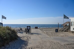 Una playa con un paseo marítimo de hormigón, mesas de picnic, una bicicleta y una estación de salvavidas.