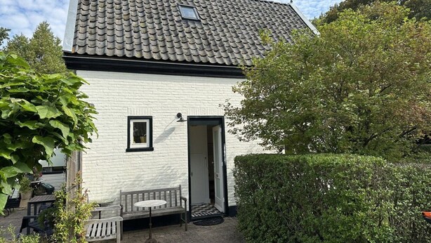 A white brick house with a tiled roof, a small window, and a door. There is a bench and a table outside. - Lovely holiday home centrally located in Bergen in delightful surroundings. (Bergen)