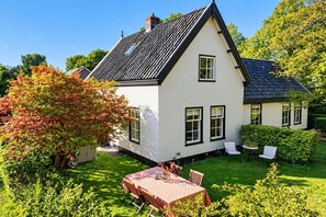 Una casa blanca con techo negro, rodeada por un jardín cuidado y un comedor con mesa y sillas.