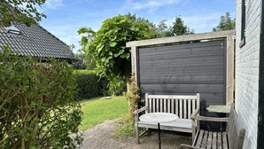 A wooden bench and table set against a dark wooden wall, with a garden path leading to a house with a tiled roof. - Lovely holiday home centrally located in Bergen in delightful surroundings. (Bergen)