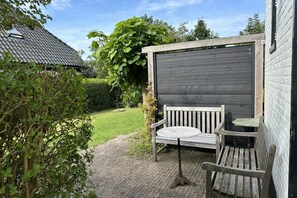 A wooden bench and table set against a dark wooden wall, with a garden path leading to a house with a tiled roof. - Lovely holiday home centrally located in Bergen in delightful surroundings. (Bergen)