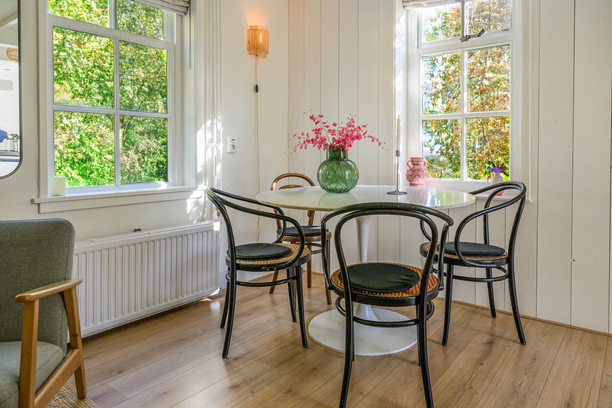 Ein Essbereich mit einem runden Tisch, vier Stühlen, einer Blumenvase und einem Fenster mit Blick auf Bäume.