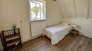 A small, single-bed room with a sloped ceiling, a window with a view of the outside, a radiator, a bedside table with a lamp, and a wooden bench. - Lovely holiday home centrally located in Bergen in delightful surroundings. (Bergen)