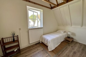A small, single-bed room with a sloped ceiling, a window with a view of the outside, a radiator, a bedside table with a lamp, and a wooden bench. - Lovely holiday home centrally located in Bergen in delightful surroundings. (Bergen)