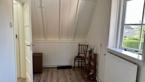 A room with a sloped ceiling, a window with a view of greenery, a radiator, and a chair. - Lovely holiday home centrally located in Bergen in delightful surroundings. (Bergen)