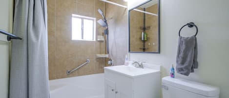 Une salle de bain équipée d’une baignoire, d’un lavabo, de toilettes, d’une pomme de douche, d’un porte-serviettes et d’un miroir.