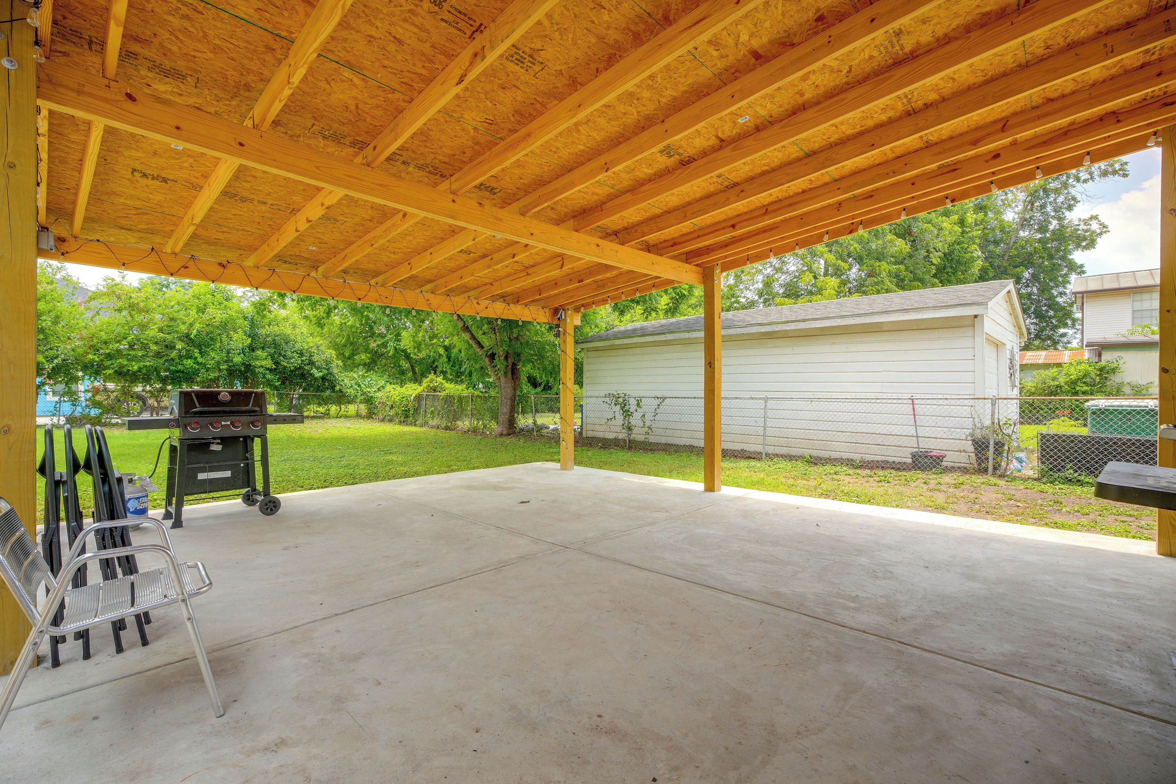 An outdoor covered patio area with a concrete floor, a grill, and a table with chairs.