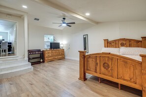 A spacious bedroom with a wooden bed, a dresser, a television, and a ceiling fan.
