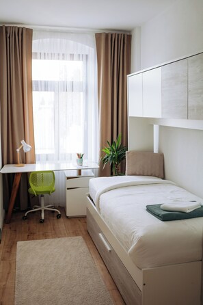 A bedroom with a bed, desk, chair, and a window with curtains. - Vrbo Property (Reichenbach im Vogtland)