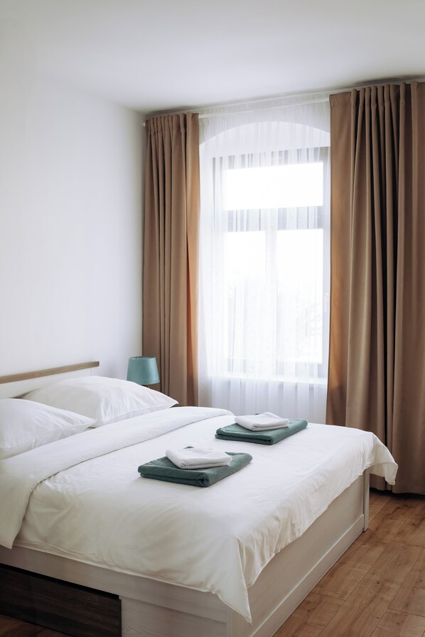 A hotel room with a bed, a nightstand, a lamp, and a window with curtains. - Vrbo Property (Reichenbach im Vogtland)
