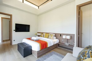 A modern hotel room with a large bed, bedside tables, a flat-screen TV, and a window with blinds. - Villa Koa 4BR at Aileen Villas Layan (Choeng Thale)