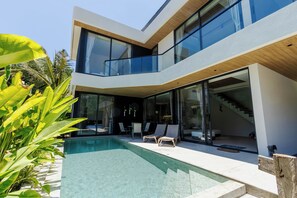 Une maison moderne à deux étages, dotée d’une piscine, de portes vitrées et d’un escalier menant à l’étage supérieur.