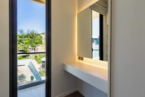 A modern bathroom with a large mirror, a white countertop, and a view of a balcony with greenery and buildings. - Villa Koa 4BR at Aileen Villas Layan (Choeng Thale)