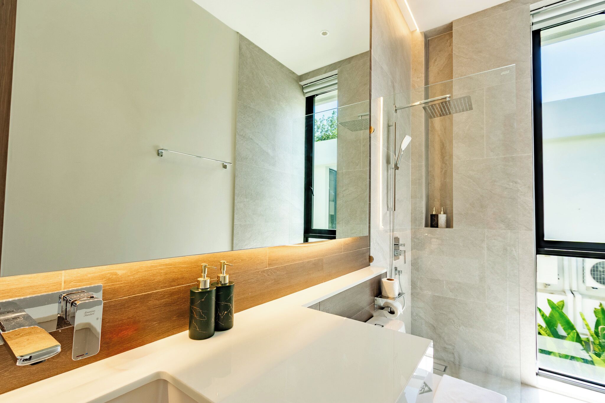 A modern bathroom with a large mirror, a shower, and a sink with soap dispensers.