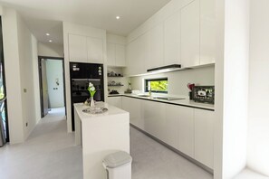A modern kitchen with white cabinetry, a black refrigerator, and a window with a view of greenery. - Villa Koa 4BR at Aileen Villas Layan (Choeng Thale)