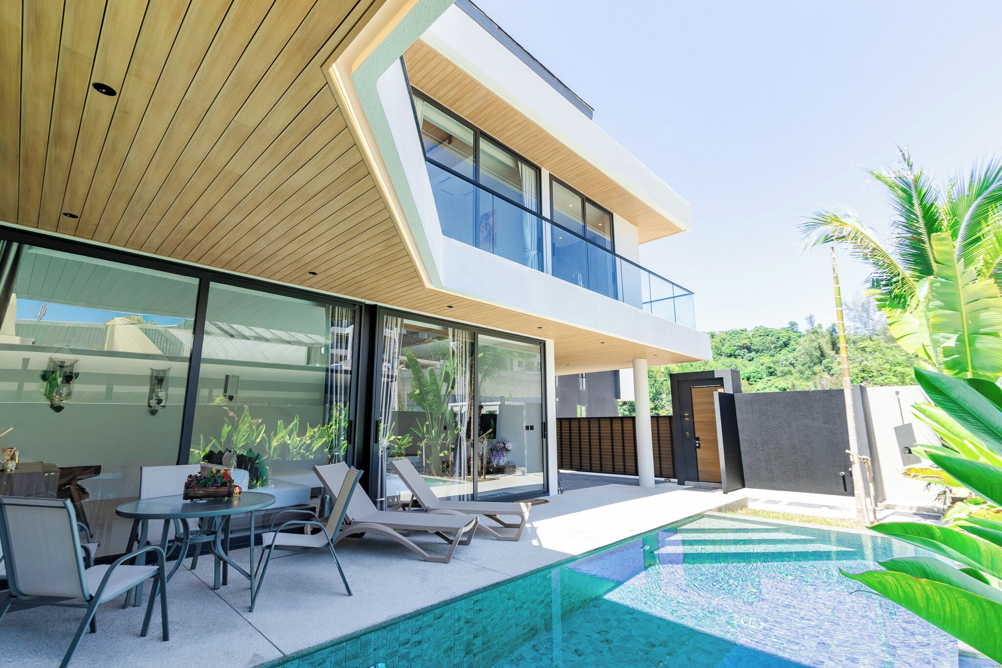 A modern two-story house with a glass facade, a pool, and outdoor seating.