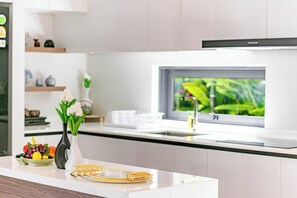 Una cocina moderna con encimera blanca, un florero con flores y una ventana con vistas a la vegetación.