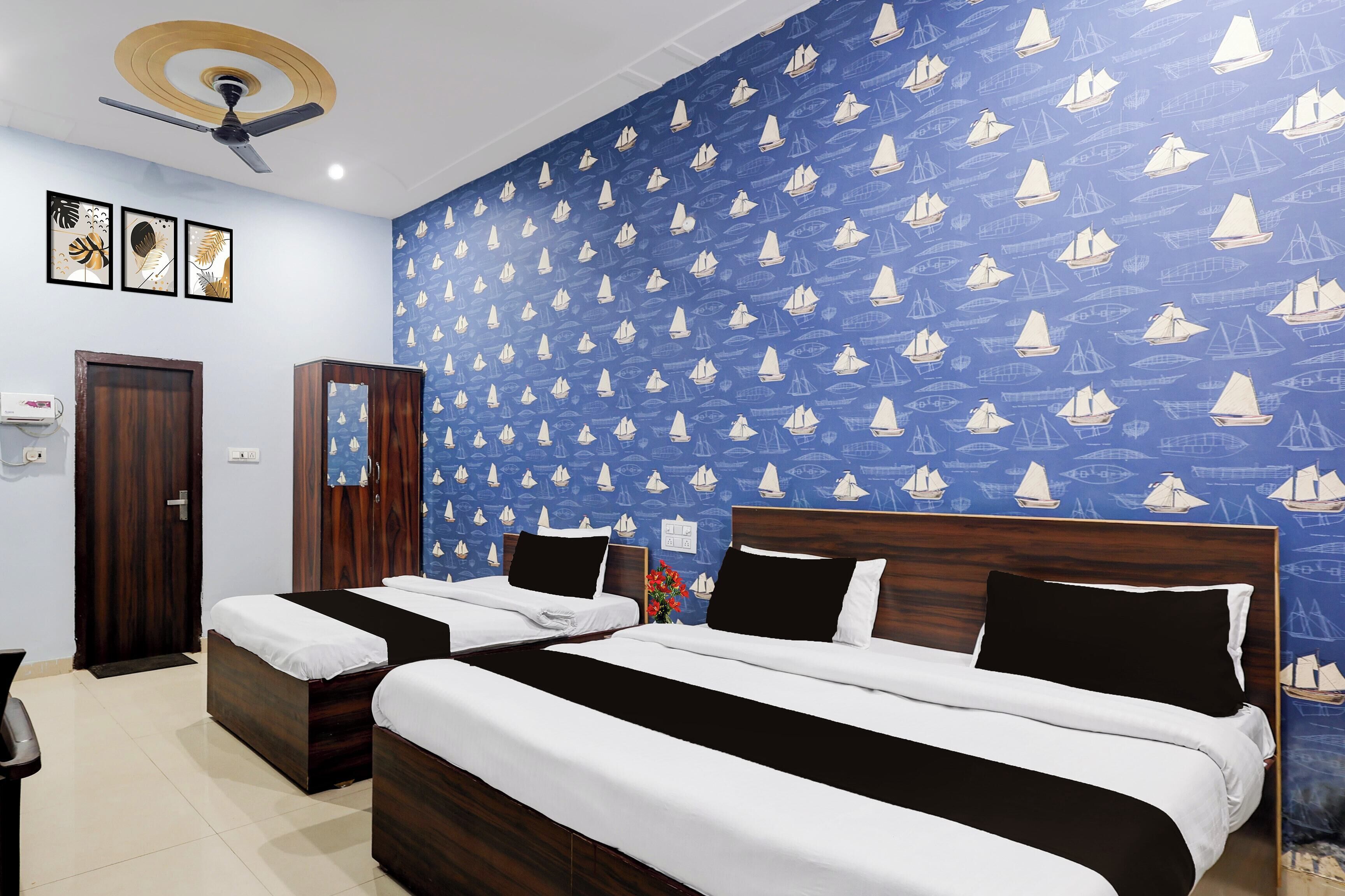 A hotel room with two beds, a ceiling fan, and a blue wall with sailboat patterns.