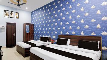 A hotel room with two beds, a ceiling fan, and a blue wall with sailboat patterns.