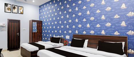 A hotel room with two beds, a ceiling fan, and a blue wall with sailboat patterns.
