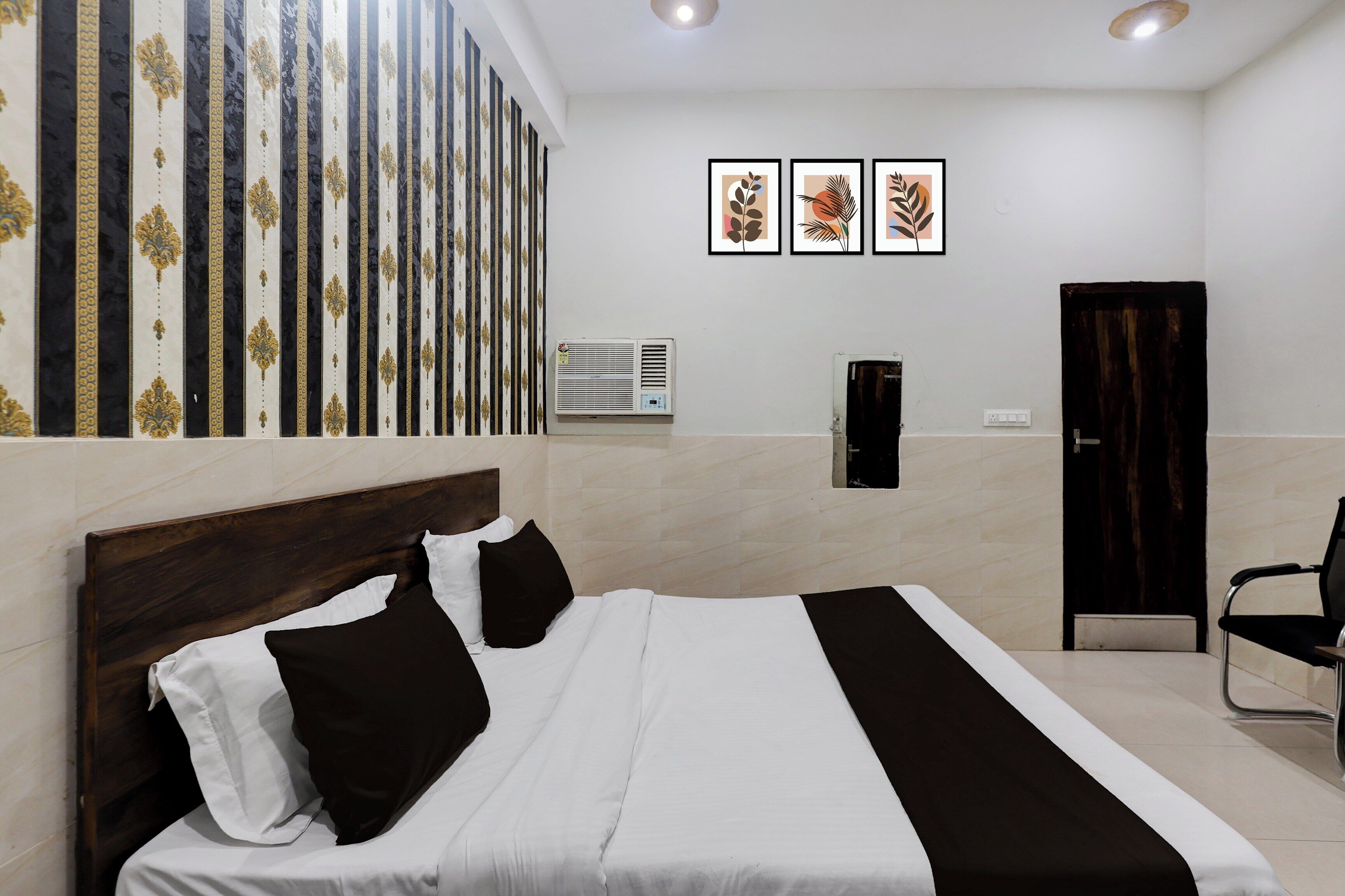 A hotel room with a bed, a chair, a wall-mounted air conditioner, and three framed pictures.