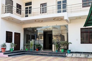 A multi-story building with a glass entrance, potted plants, and a balcony with metal railings.