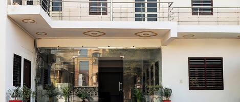 A multi-story building with a glass entrance, potted plants, and a balcony.