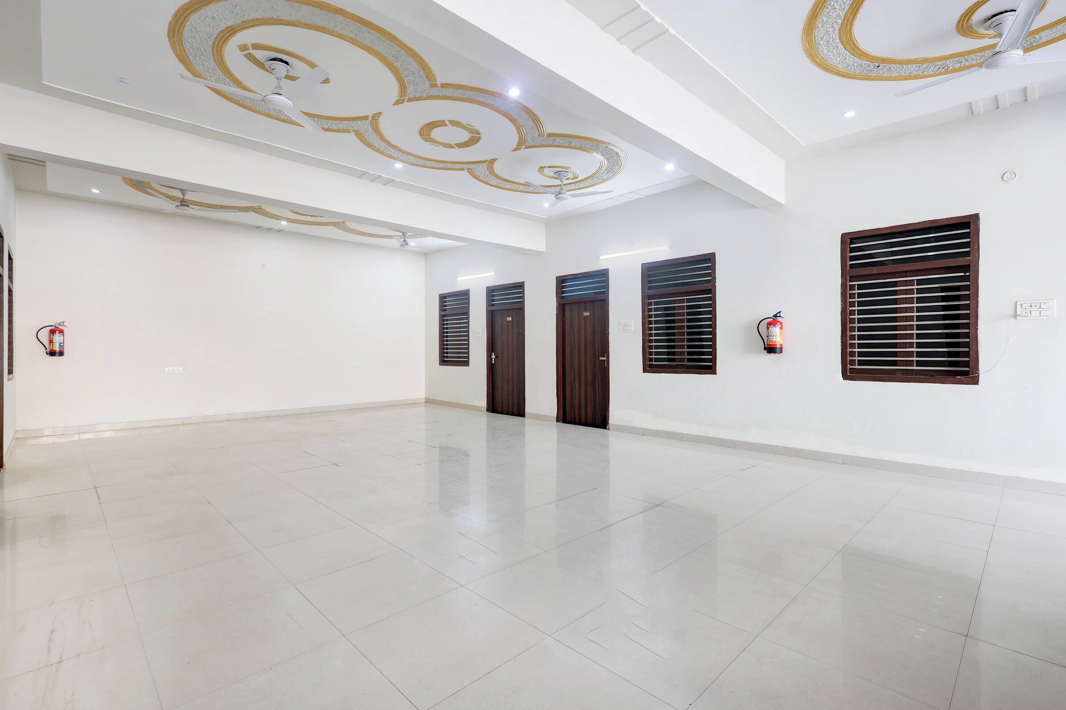 A spacious, well-lit room with a polished floor, decorative ceiling, and a fire extinguisher mounted on the wall.