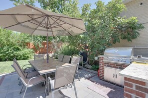 Um pátio externo com mesa, cadeiras, churrasqueira e um grande guarda-sol.
