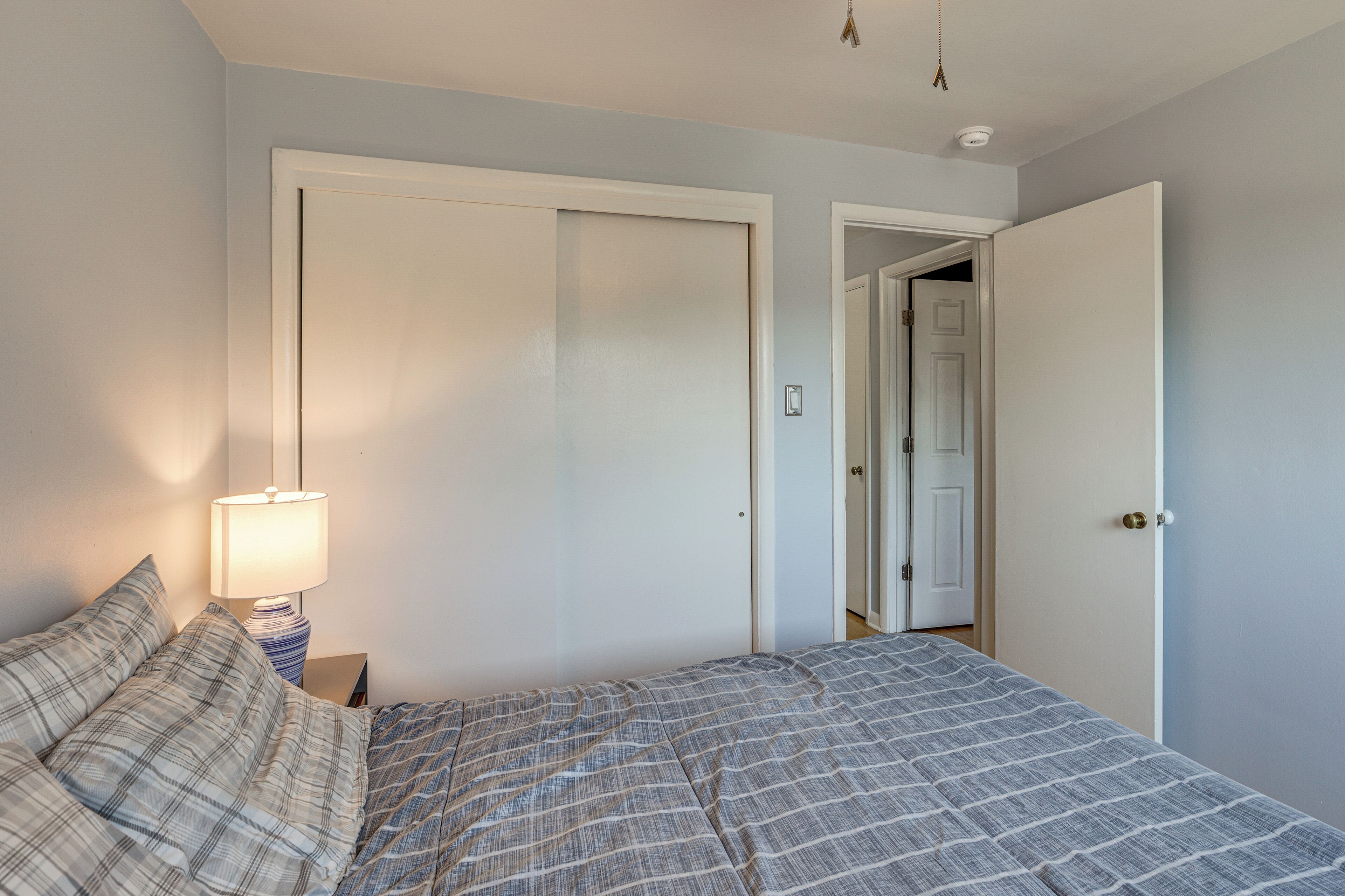 A bedroom with a bed, a nightstand, a lamp, and a door leading to another room.