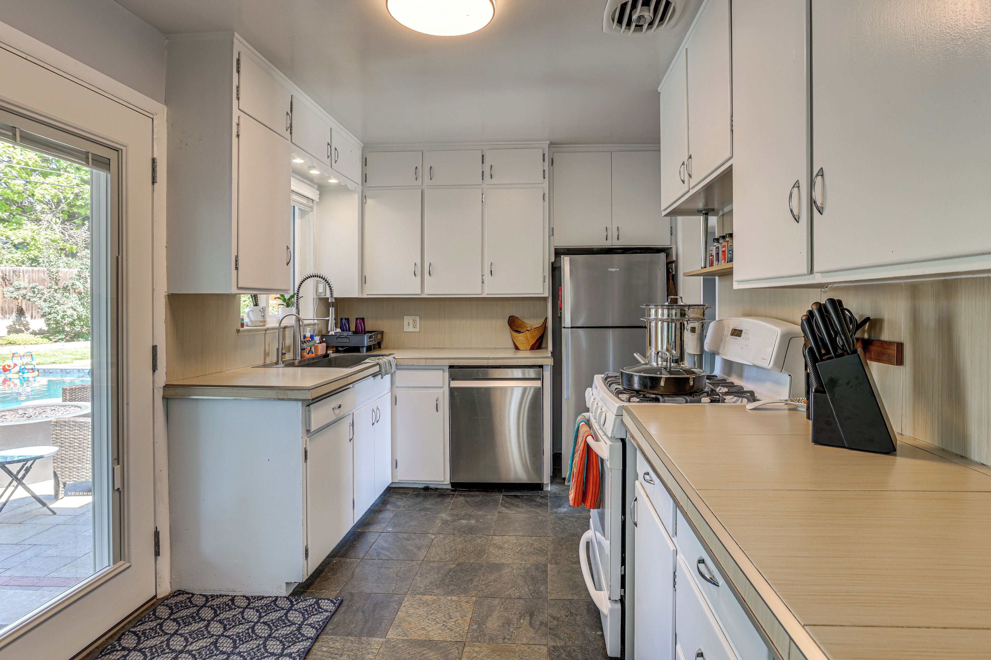 A modern kitchen with white cabinets, stainless steel appliances, and a view to the outside.