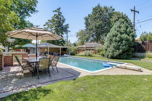 Um quintal com piscina, móveis de pátio e área para churrasco.