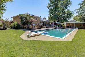 Un patio trasero con piscina, mobiliario de jardín y una zona de barbacoa cubierta.
