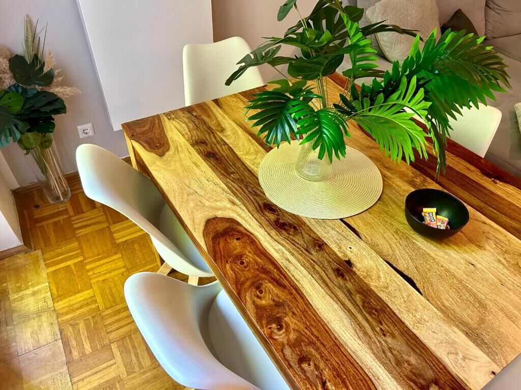A dining table with a wooden top, surrounded by white chairs, and a potted plant.
