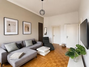A modern living room with a grey sofa, a black lounge chair, a white coffee table, and a large flat-screen TV. - New Villa Apartment, Sleeps 6, Balcony, Ideal for Football Teams Schalke 04! (Gelsenkirchen)