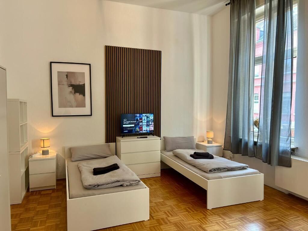 Una habitación de hotel moderna con una cama, mesitas de noche, televisión y ventana con cortinas.