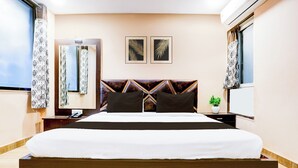 Ein Hotelzimmer mit einem großen Bett, einem Nachttisch mit Telefon, einer kleinen Pflanze und zwei gerahmten Blätter-Kunstwerken an der Wand.