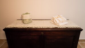 Een donkere houten ladekast met een wit kantkleed en een groene kussens erop.