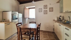 Een keuken met een houten tafel, stoelen, een inbouwoven en een raam met gordijnen.
