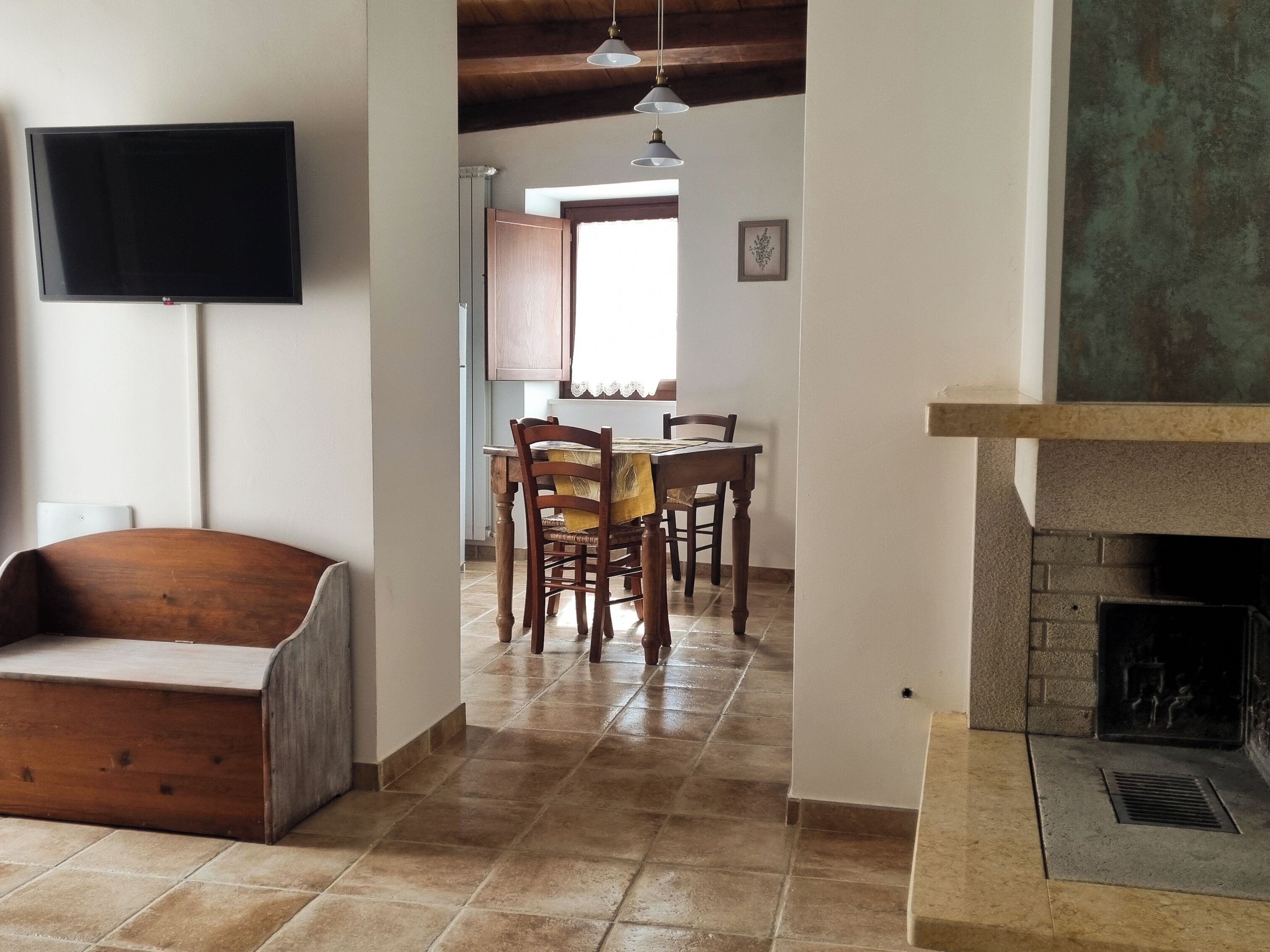 Una sala de estar con chimenea, un comedor con sillas de madera y una mesa, y un televisor montado en la pared.